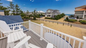 Une propriété située en bord de mer, dotée d’une terrasse en bois, d’une vue sur la plage et d’un bâtiment à deux étages avec un balcon.