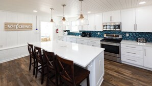 Une cuisine moderne avec des meubles blancs, un grand îlot central doté de tabourets, des appareils en acier inoxydable et un dosseret de carrelage bleu.