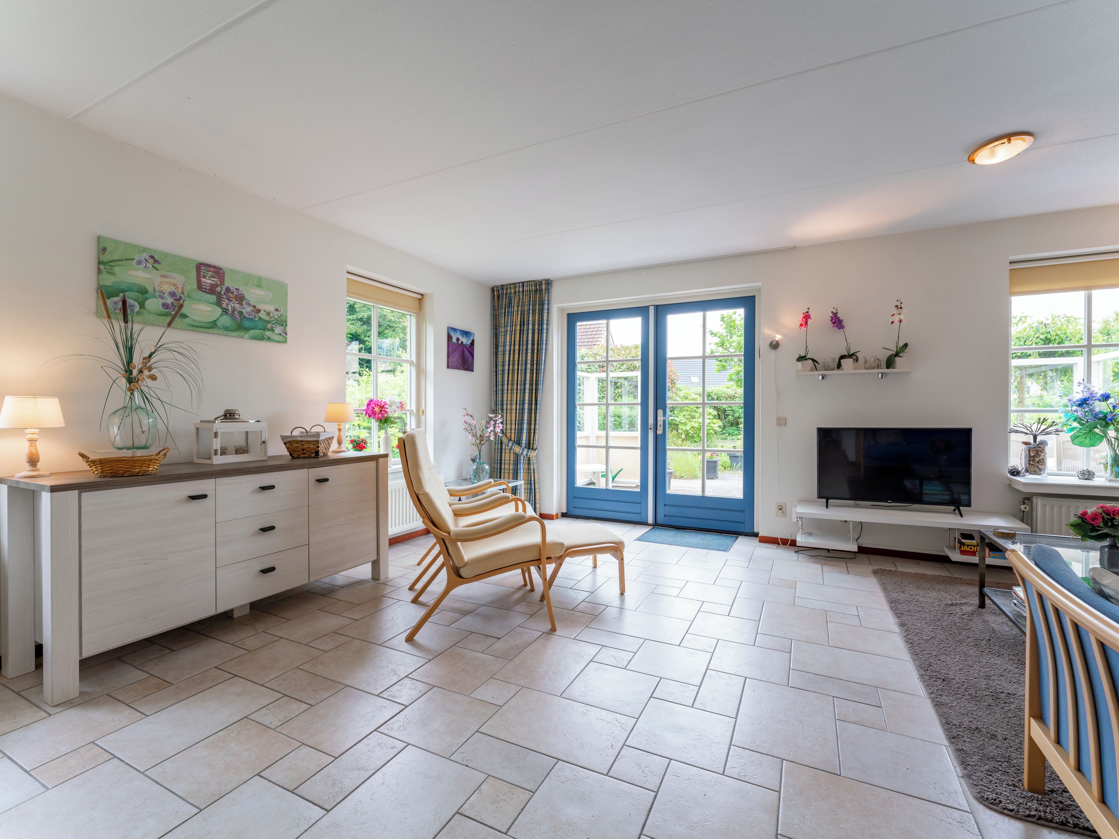 A spacious living room with a large TV, a dining area with a table and chairs, and a kitchen area with a fridge and cabinets.