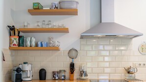 Cocina con alacenas blancas, cafetera, tetera y diferentes vasos sobre la encimera.