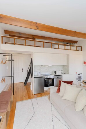 A compact living space with a kitchenette, a sofa, a bench, and a staircase leading to an upper level.