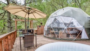 Une terrasse en bois avec un jacuzzi, un espace salon couvert avec des chaises et une structure en forme de dôme géodésique.