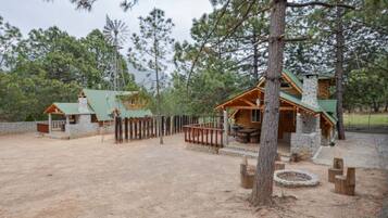 A rustic cabin with a stone chimney, wooden deck, and a fenced area with a fire pit.