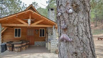 A rustic cabin with a wooden exterior, stone accents, and a large tree with carved animal faces.
