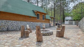 Een vakantiehuis in blokhutstijl met een stenen fundering, een houten terras en een vuurplaats van steen.