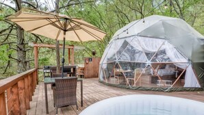 Une terrasse en bois avec un jacuzzi, un espace salon couvert et une structure en forme de dôme géodésique.