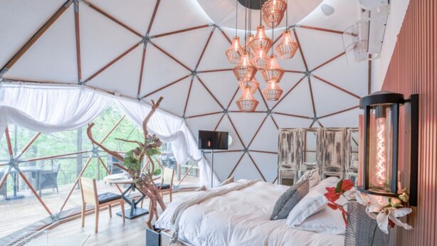 Un hébergement sous tente comprenant un lit, des lampes suspendues et une vue sur l’extérieur.
