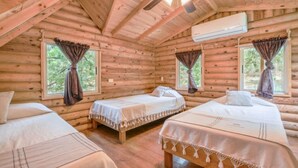 A log cabin room with two beds, a ceiling fan, and an air conditioning unit.