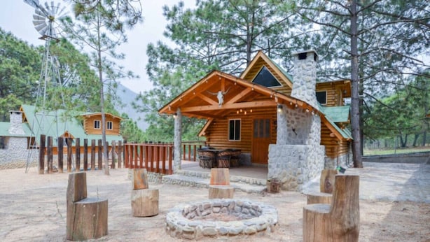 A rustic cabin with a stone chimney, wooden deck, and a fire pit.