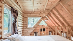 A log cabin bedroom with a bed, a window with curtains, and a skylight.