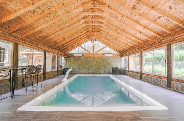 Une piscine intérieure avec des poutres en bois, des murs en pierre et de grandes fenêtres.