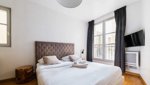 Un dormitorio con una cama grande, una televisión de pantalla plana, un ventanal con cortinas y suelo de madera.
