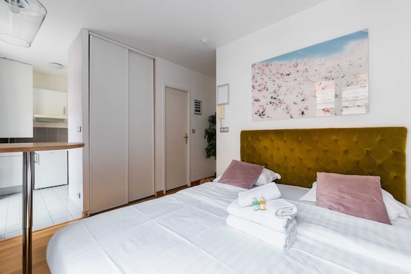 Une chambre d’hôtel avec un lit, une tête de lit, un tableau et une porte.