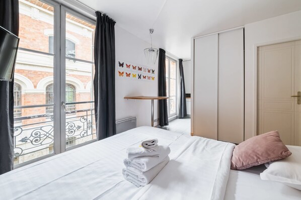 A hotel room with a bed, a window with curtains, a wall-mounted butterfly decoration, and a door.