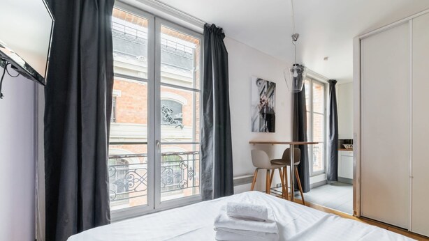 A hotel room with a bed, a desk, a chair, and a view of the outside balcony.