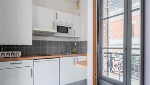 A modern kitchen with white cabinets, a microwave, and a dishwasher. There is a window with a view of a balcony.