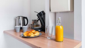 A kitchen counter with a coffee maker, croissants, a glass, and a juice bottle.