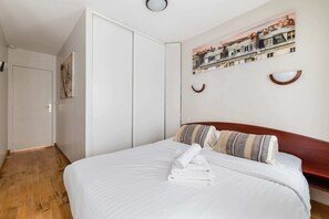 Une chambre d’hôtel avec un lit, un plancher en bois, une porte blanche et un tableau représentant un paysage urbain accroché au mur.