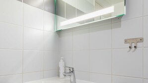 Une salle de bain avec un lavabo blanc, un miroir et un luminaire placé au-dessus du miroir.