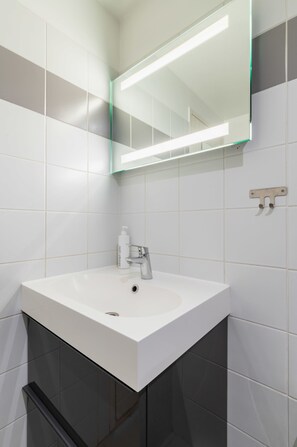 Un baño con lavamanos blanco, un espejo y una lámpara sobre el espejo.