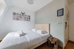 Una cama bien hecha con ropa blanca, un televisor de pared y una colección singular de platos.