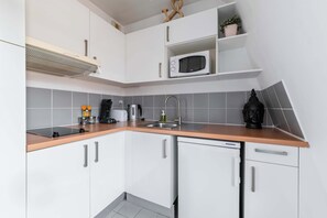 Una cocina con armarios blancos, microondas, fregadero y cafetera.