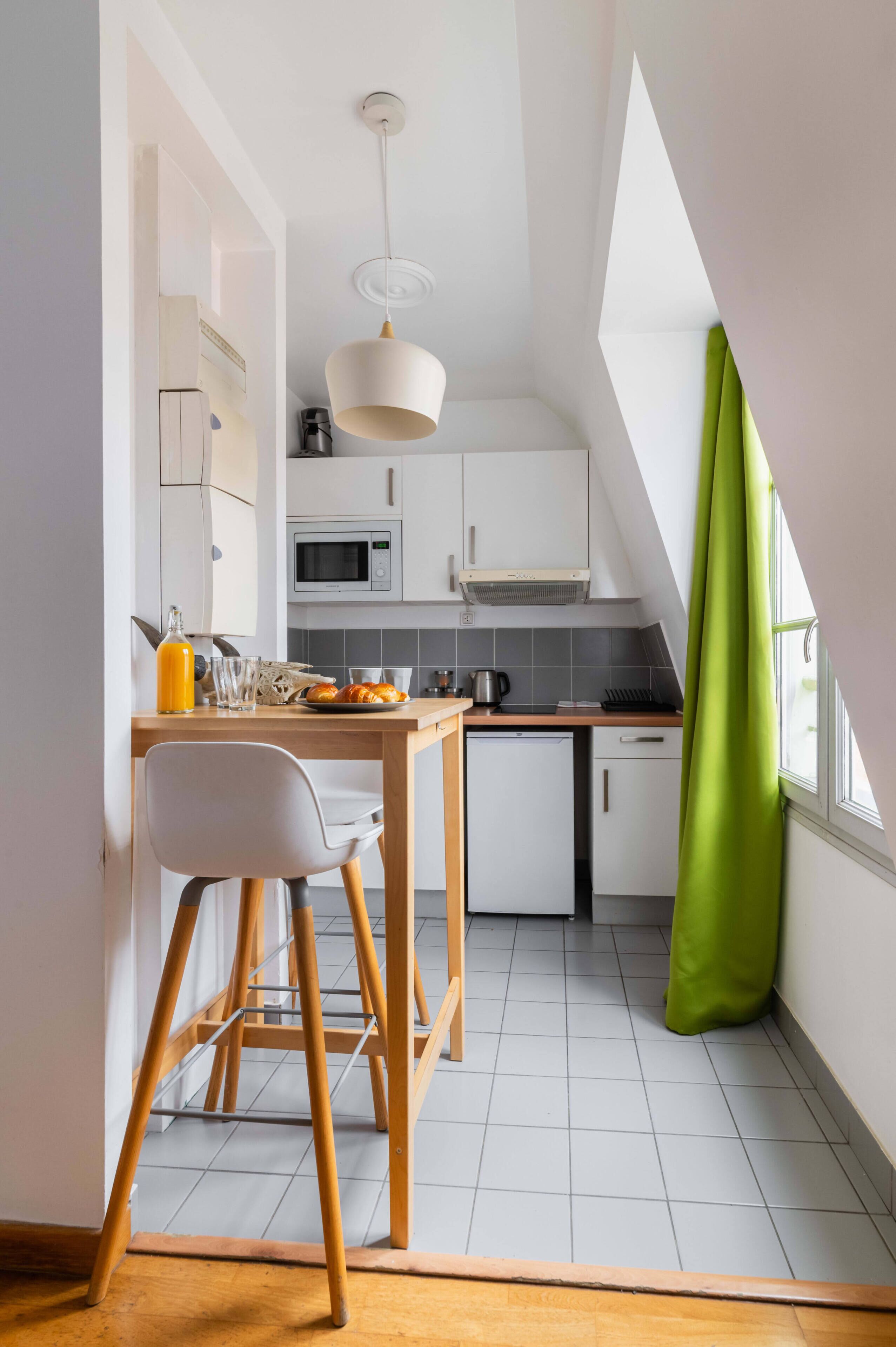 Une cuisine avec des meubles blancs, une table en bois et un rideau vert.