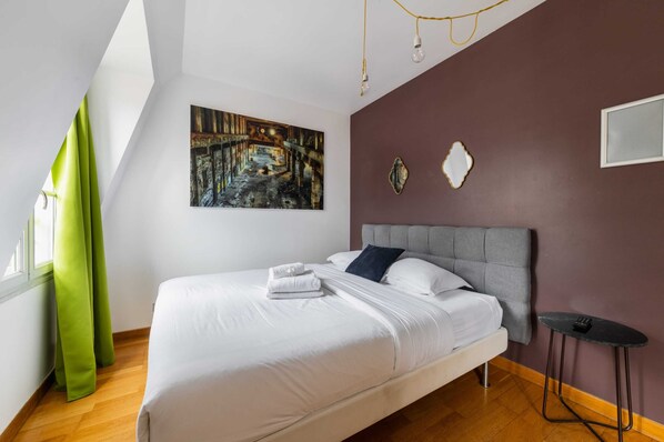Une chambre à coucher moderne avec un lit, un tableau, une petite table et une chaise.
