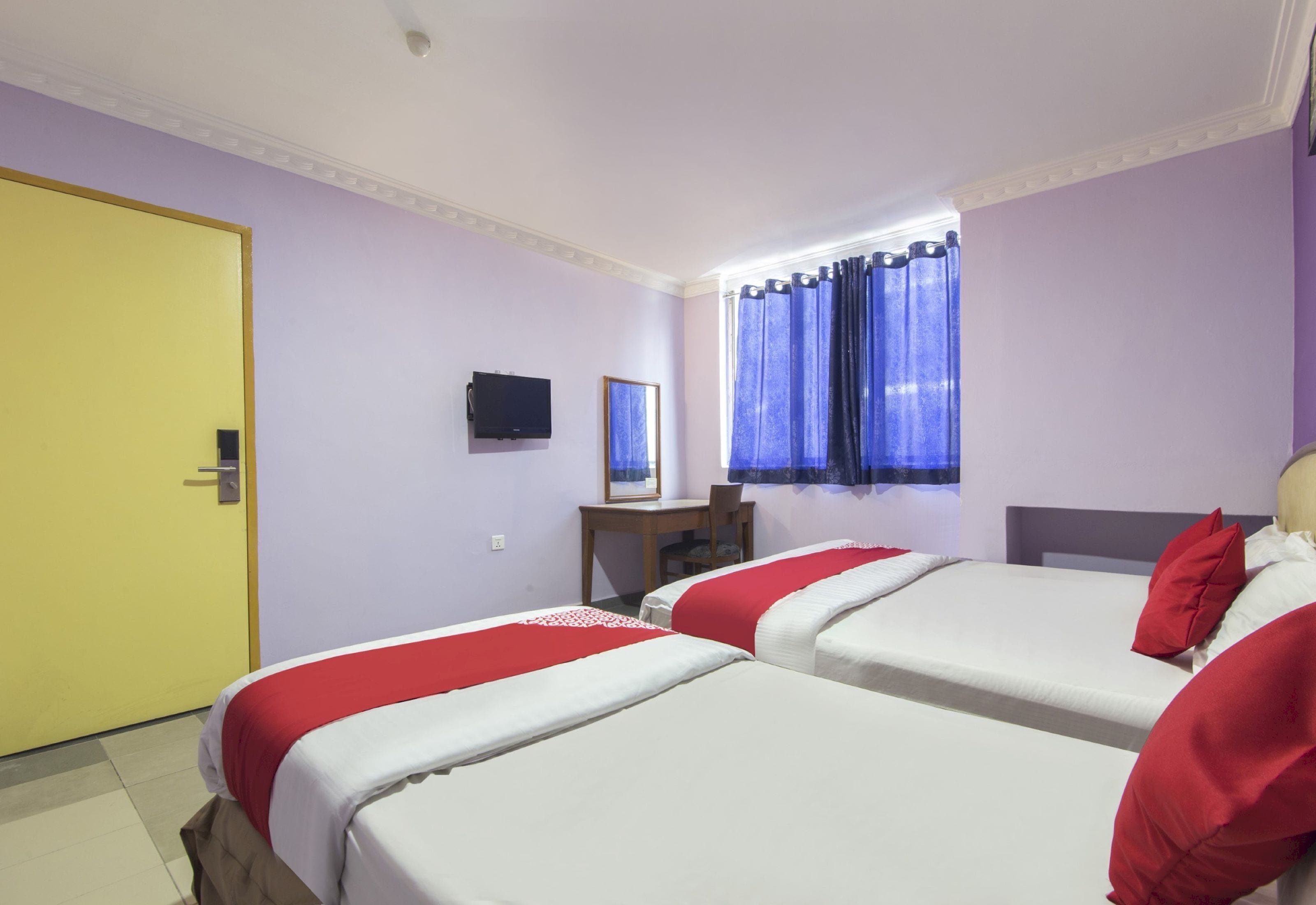 A hotel room with two beds, a desk, a television, and a window with curtains.