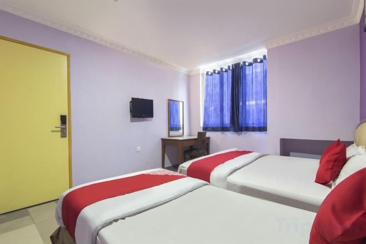 A hotel room with two beds, a desk, a chair, a television, and a window with curtains.