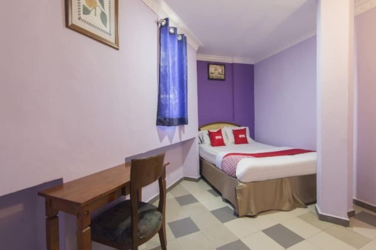 Una habitación pequeña con una cama, una silla, una mesa y una ventana con cortinas azules.