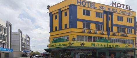 Un hotel de varios pisos con fachada amarilla y azul, un restaurante llamado M. Tasleem en la planta baja, y un letrero que dice 'Vivo' en el edificio contiguo.