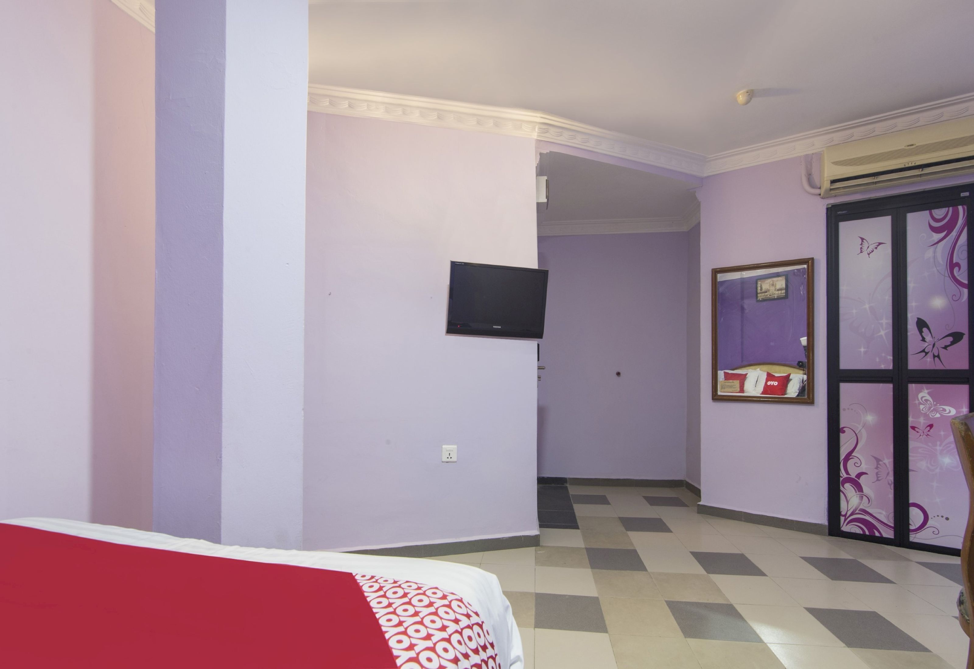 A hotel room with a bed, a television mounted on the wall, a window with decorative glass, and a checkered floor.