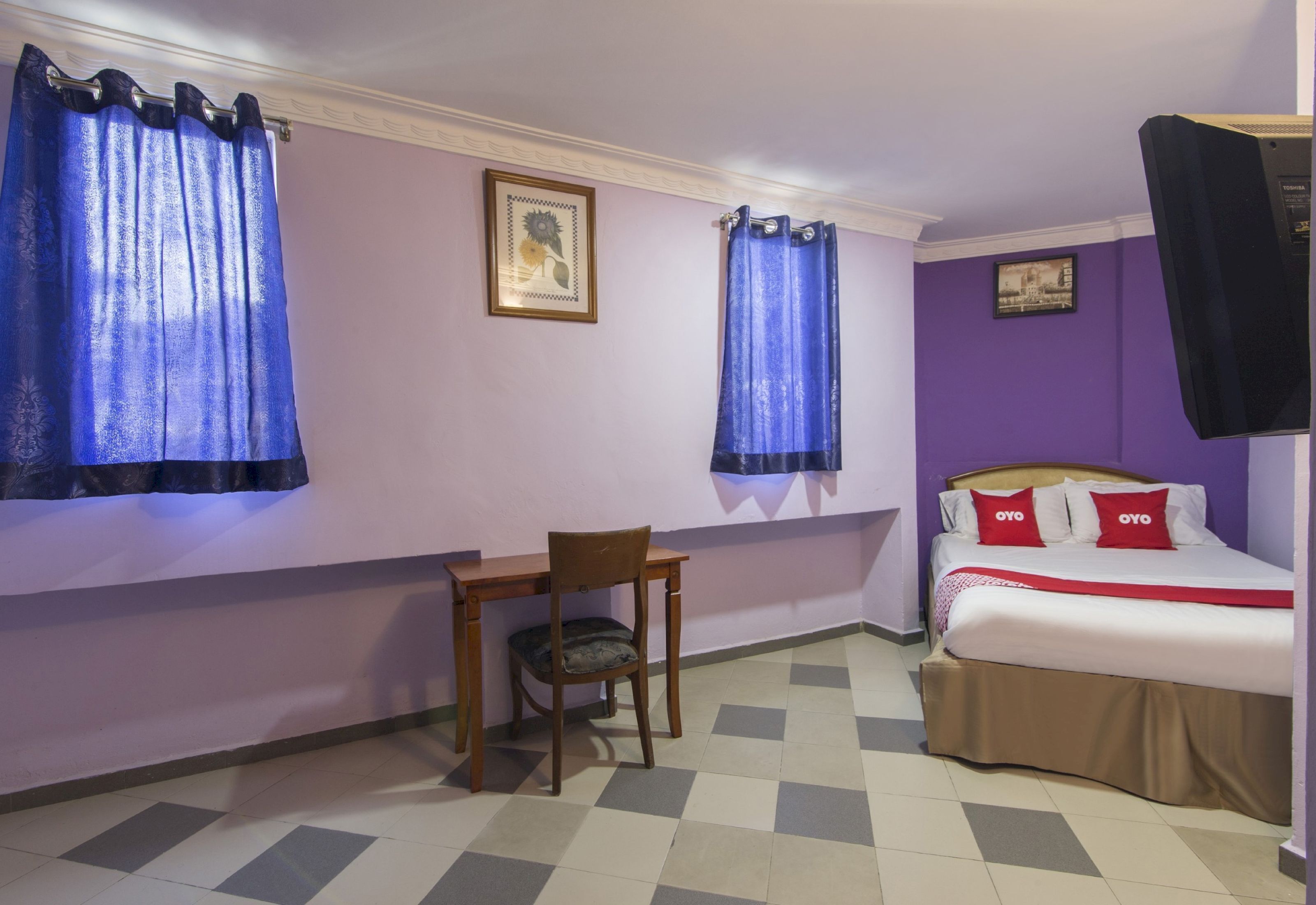 A room with a bed, a desk, and two windows with blue curtains.