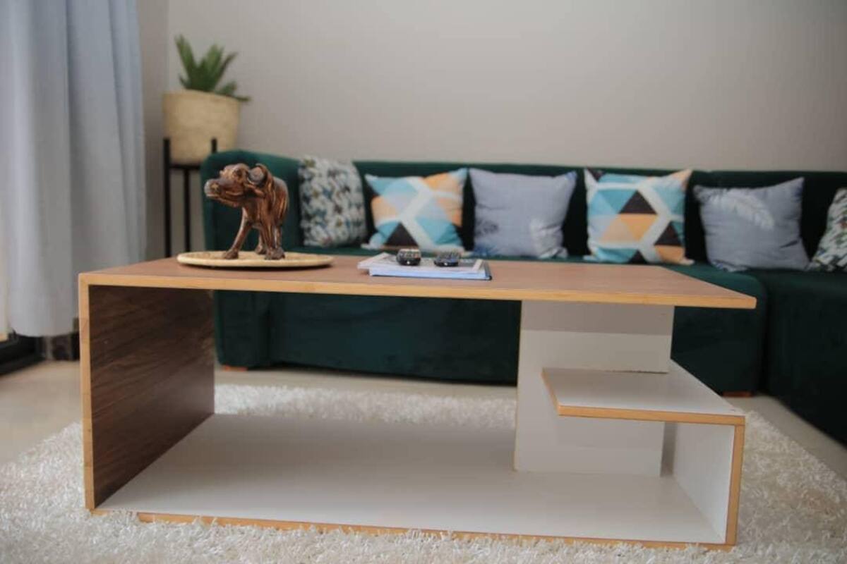 Un salon moderne avec une table basse en bois, une petite sculpture et un canapé vert agrémenté de coussins à motifs.