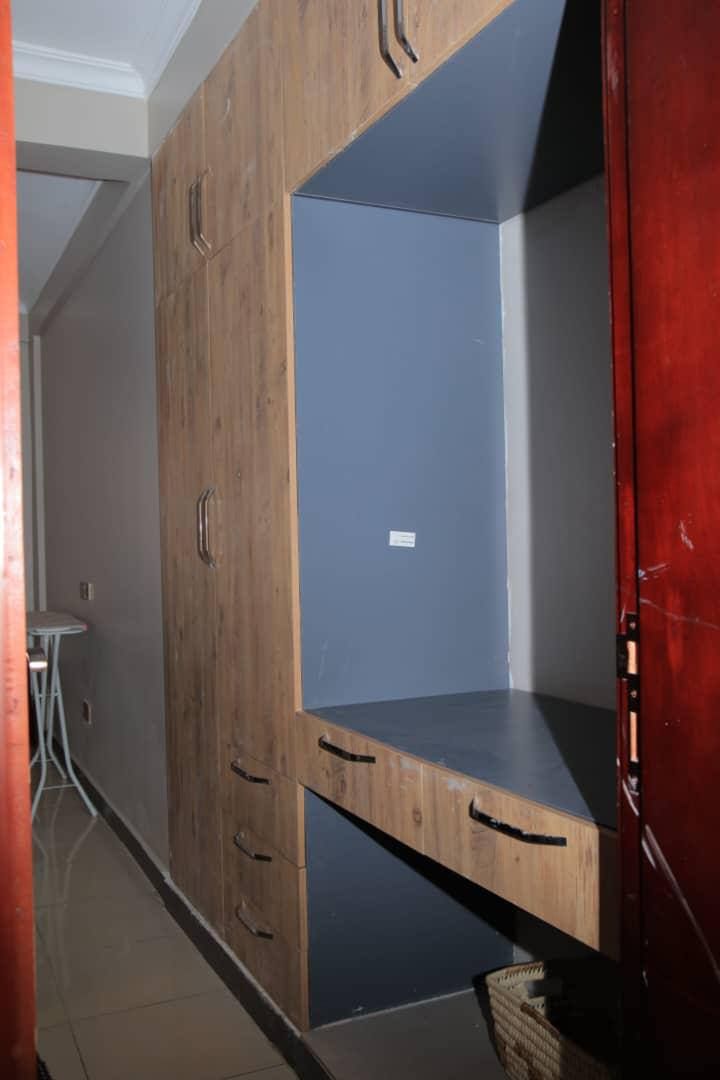 A room with a wooden wardrobe, a desk, and a red door.