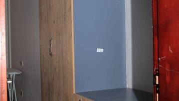 A room with a wooden wardrobe, a desk, and a red door.
