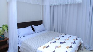 Een slaapkamer met een bed, witte gordijnen, een baldakijn en een kamerplant.