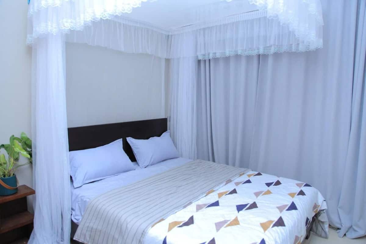Une chambre à coucher avec un lit, des rideaux blancs, un baldaquin et une plante en pot.