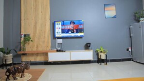 Een receptiegedeelte met een wand van houten panelen, een televisie waarop een MotoGP-evenement draait, een kleine plant en een decoratief keramiekbeeldje.