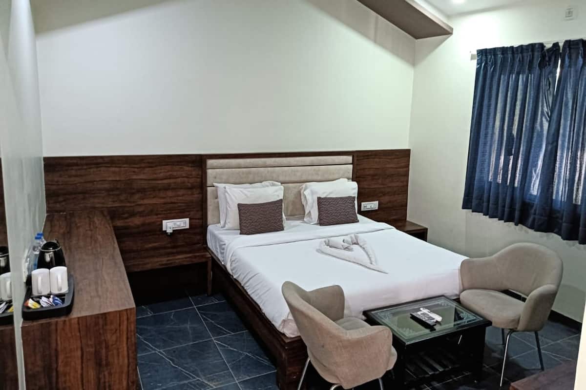 Una habitación de hotel con cama, dos sillas, una mesita, una mesita de noche y una cortina.