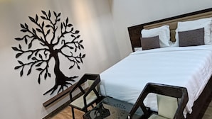 Une chambre à coucher avec un lit, des oreillers, un motif décoratif représentant un arbre appliqué sur le mur et une chaise.