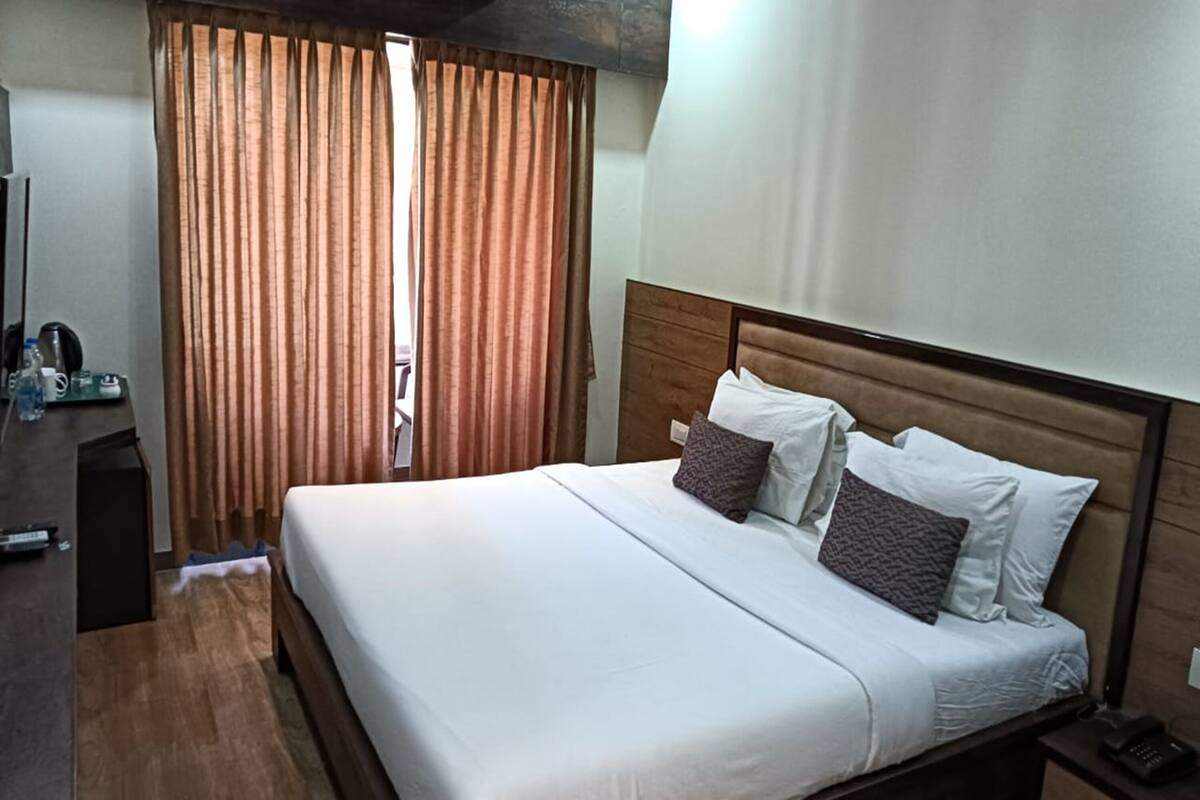 Una habitación de hotel con una cama de madera, ropa de cama blanca y cabecero de madera. Hay un escritorio con un teléfono y una botella de agua.