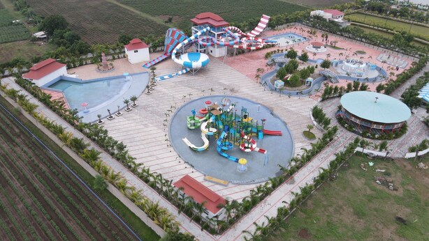Vue aérienne d’un parc d’attractions avec diverses attractions et manèges, notamment un grand toboggan aquatique, des montagnes russes et un bâtiment circulaire surmonté d’un toit végétalisé.