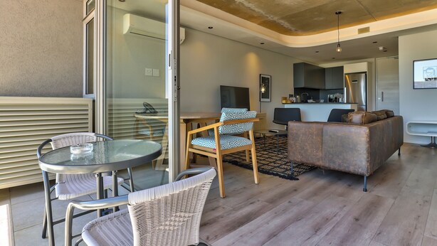 Un salon moderne avec une table en verre, des fauteuils en osier, un canapé et un coin cuisine à l’arrière-plan.