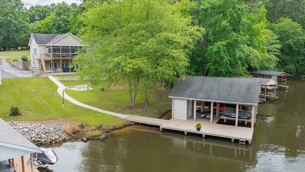 A lakeside cabin with a dock, a covered outdoor seating area, and a house in the background. - New! Family time. Hot Tub, Pool Table, Firepit, Dock, Kayaks. Screened Porch (Bracey)