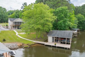 A lakeside cabin with a dock, a covered outdoor seating area, and a house in the background. - New! Family time. Hot Tub, Pool Table, Firepit, Dock, Kayaks. Screened Porch (Bracey)