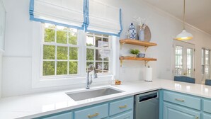 A kitchen with light blue cabinets, a white countertop, a stainless steel sink, and a window with blue curtains. - New! Family time. Hot Tub, Pool Table, Firepit, Dock, Kayaks. Screened Porch (Bracey)