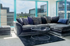Uma sala de estar moderna com sofá modular, mesa de centro e grandes janelas com vista para a cidade.