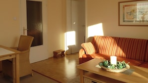 A living room with a sofa, a small table with a candle and greenery, a wicker chair, and a door. - Ferienwohnung Lehmann 58 qm, Erdgeschoss, mit Terrasse und Separatem Schlafzimmer (Bad Endorf)